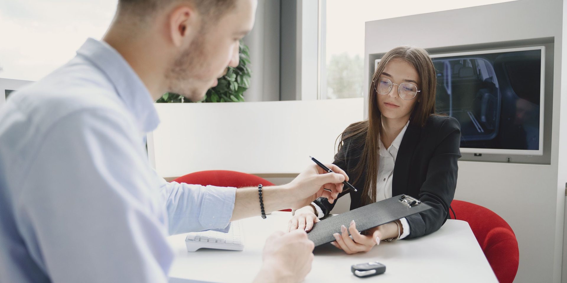 Driver signing documents at a dealership desk with the car key on the table