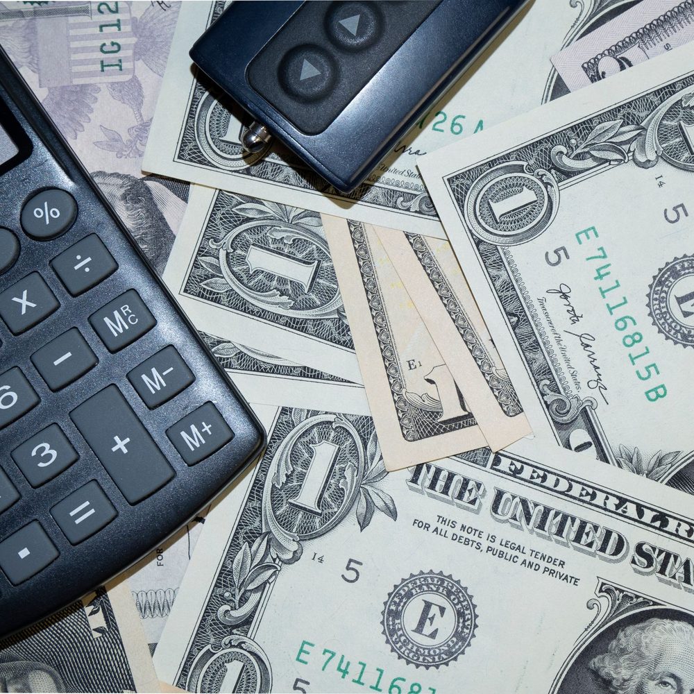 Calculator, car key fob and dollar bills on a table